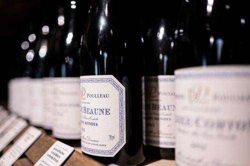 Wine bottles lined up on a shelf, with white and blue labels visible in the foreground.