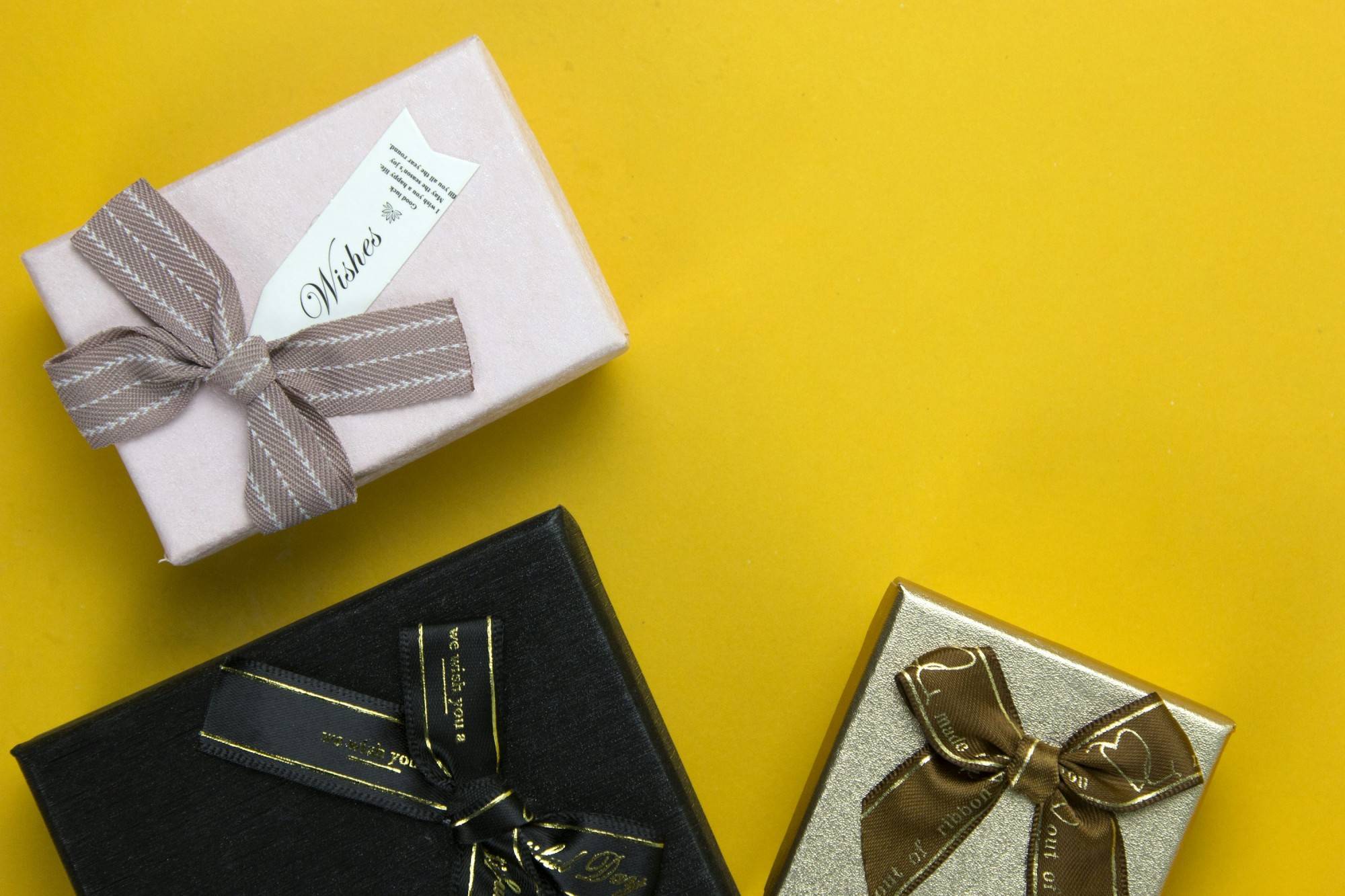 Personalisierte Geschenke, verpackt in bunten Schachteln mit Schleifen, vor gelbem Hintergrund.